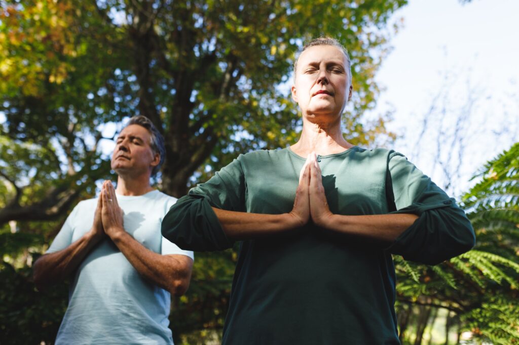 Peaceful senior caucasian couple practicing yoga, meditating in sunny garden